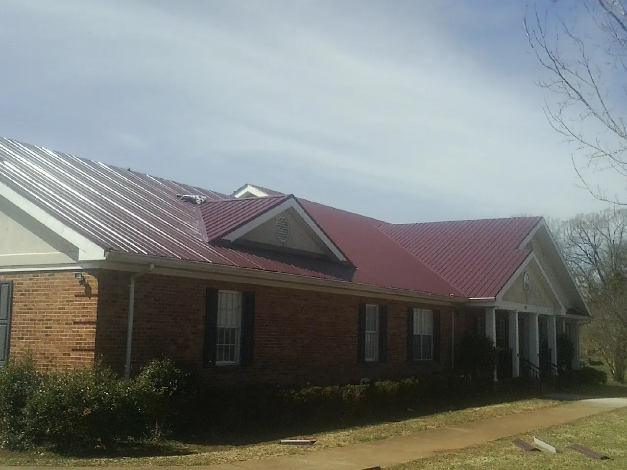 Red metal roof with gabled entries on a long brick building, from a Hail Damage Roof Repair job in New Buffalo