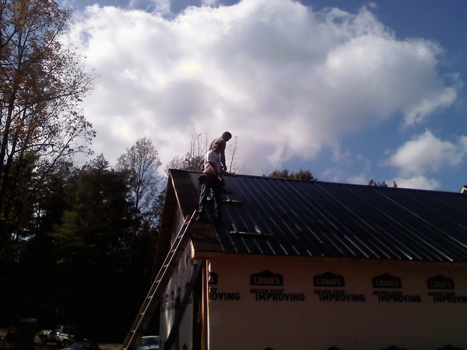 Roofer fastening dark metal panels high against a cloudy sky, from a Roof Inspection job in New Buffalo