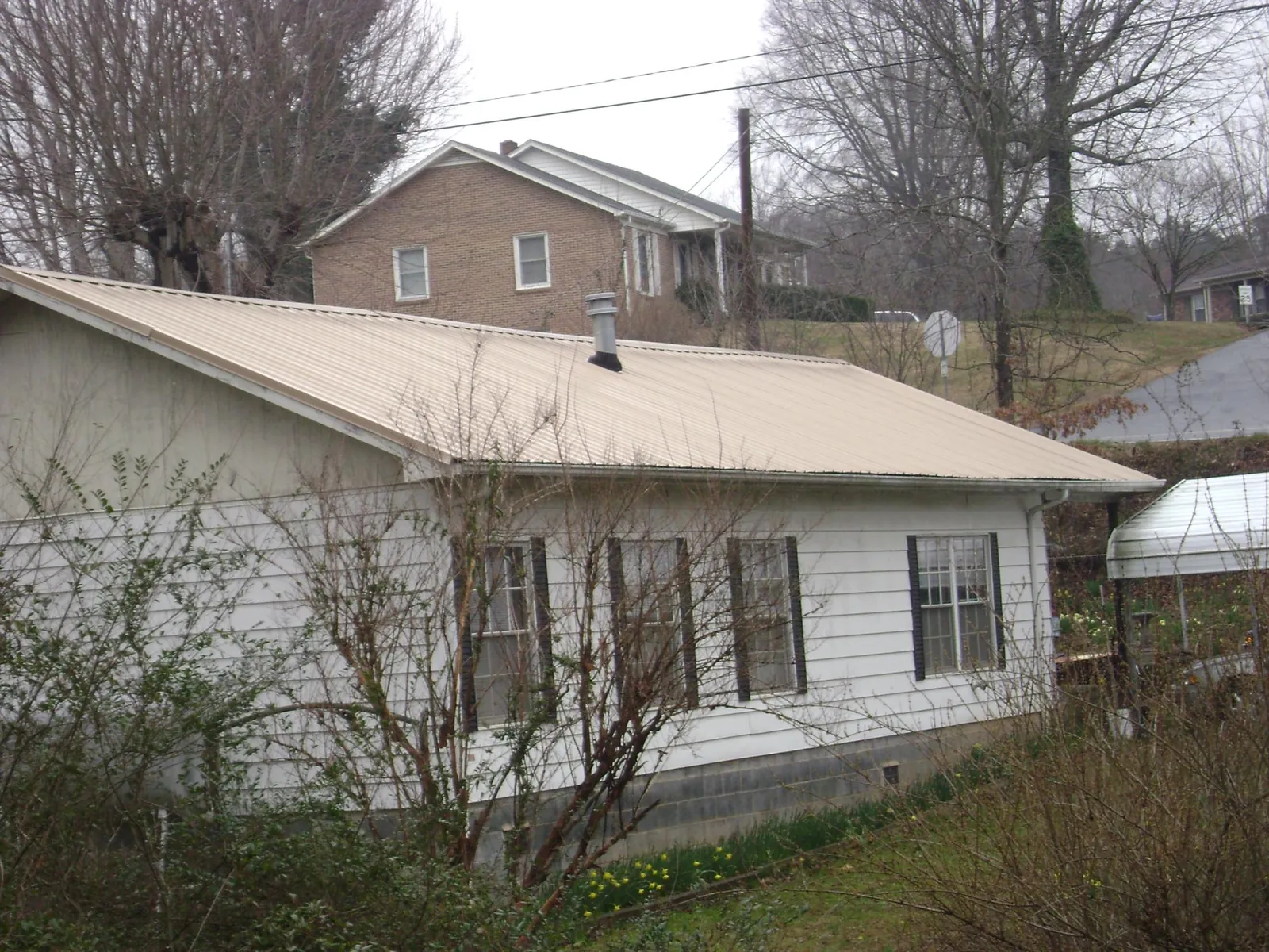 Tan metal roof on a white sided house set into a hillside — Commercial Roofing by Roofing Brothers in New Buffalo