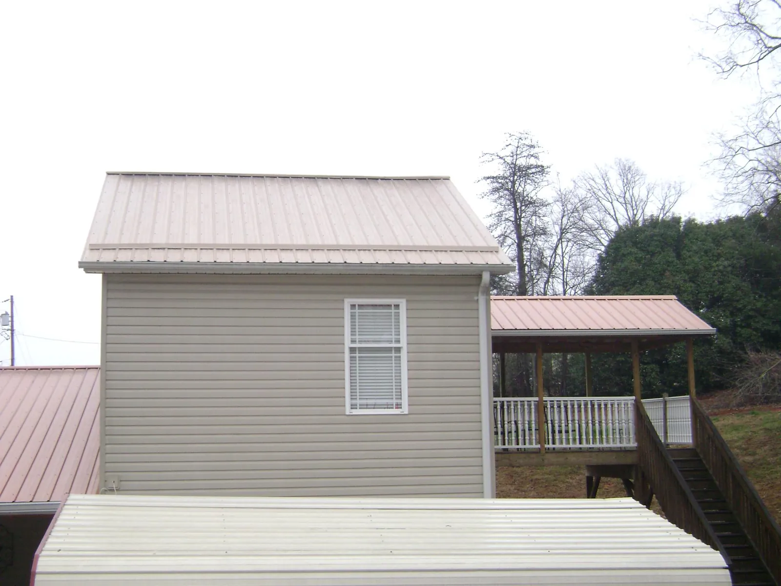 Tan metal roofs on a two story addition and attached porch, from a Roof Replacement job in New Buffalo